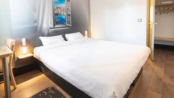 Ein Hotelzimmer mit einem großen Bett, Nachttischen mit Lampen, Blick auf eine Stadtansicht durch ein Fenster und einem Holzboden.