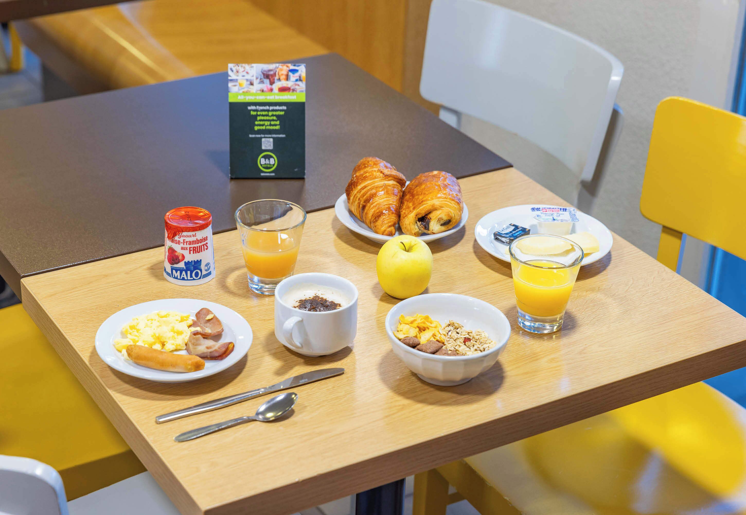 Een ontbijttafel met croissants, fruit, ontbijtgranen en sap.