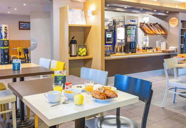 A breakfast setup with croissants, orange juice, and cereal on a table. - B&B HOTEL Saint-Malo Centre (Saint-Malo)