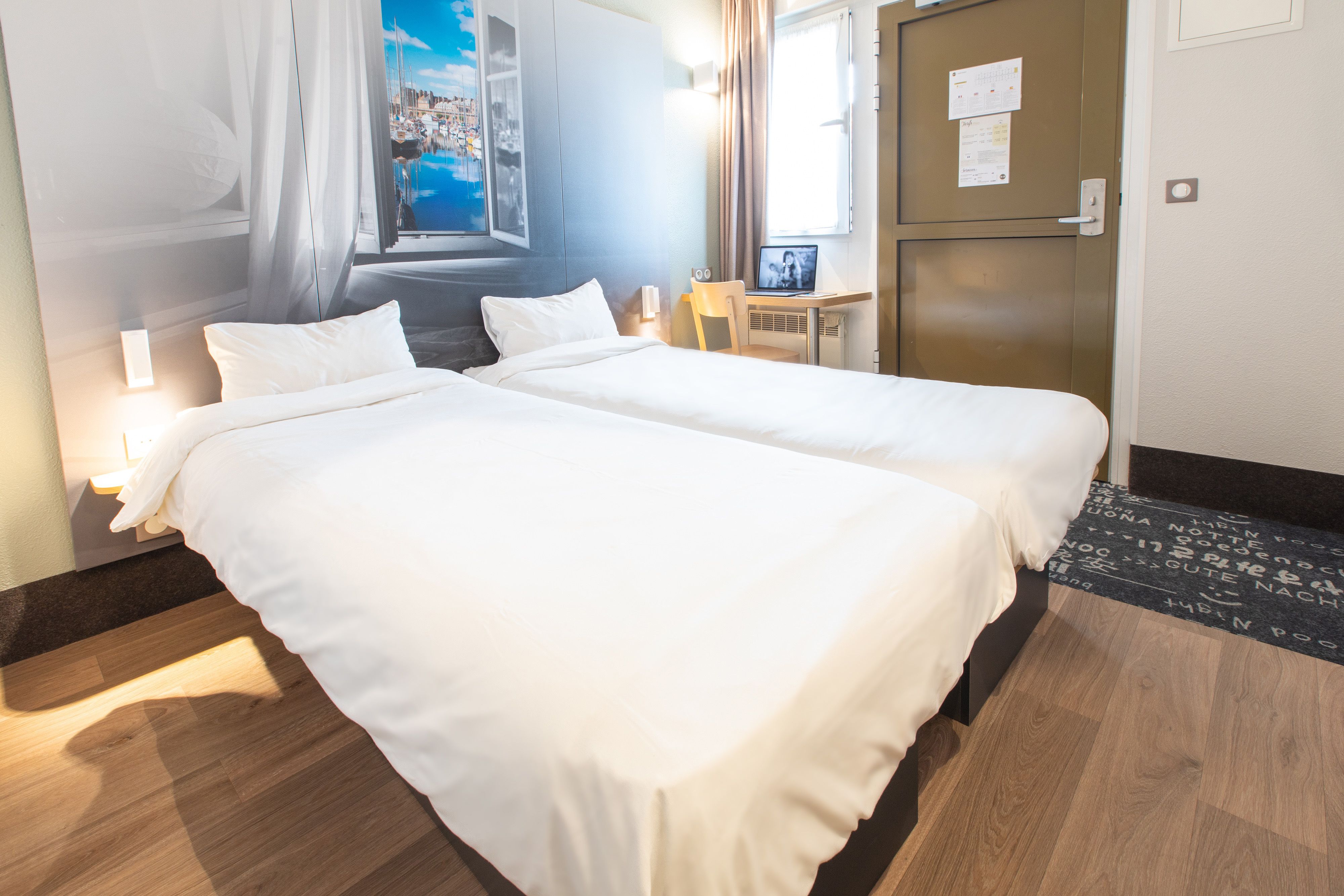 Habitación de hotel con dos camas, un escritorio, una silla y ventana con vista a la ciudad.