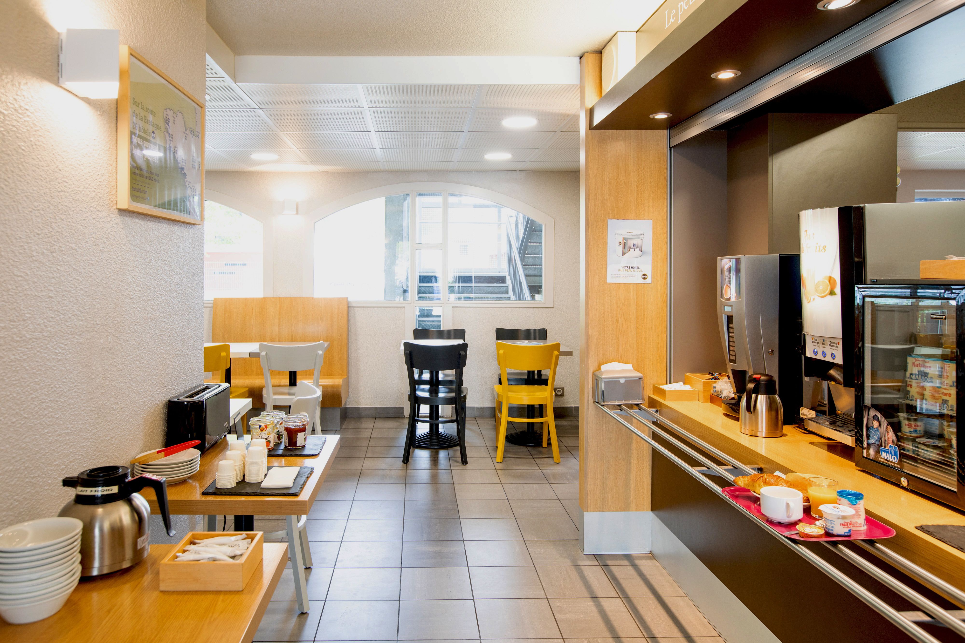 A modern hotel breakfast area with a counter, seating, and a view of the outside.