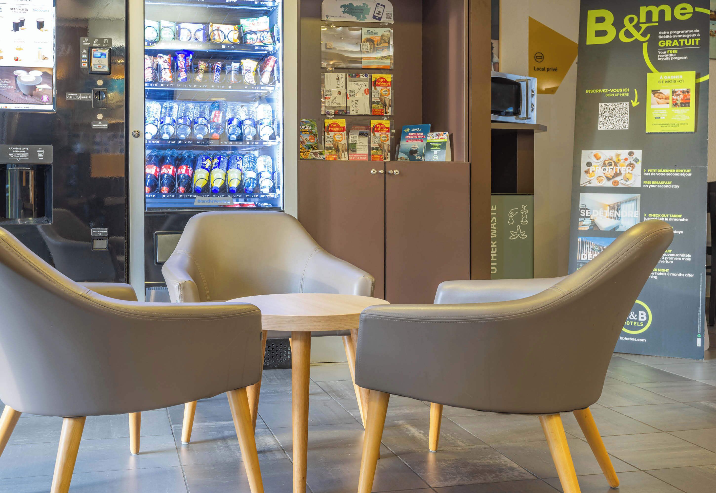A seating area with two chairs and a small table, a vending machine with beverages, and promotional posters on the wall.