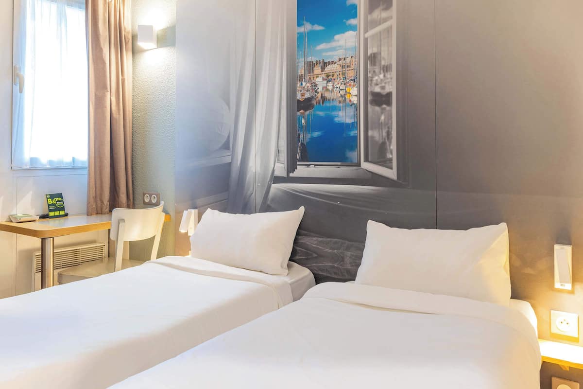 A hotel room with two beds, a desk, and a large window with a view of a marina.