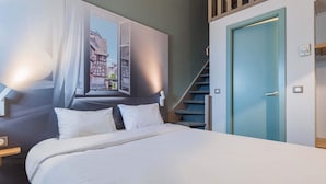 A hotel room with a bed, a window with curtains, a view of buildings, a blue door, and a staircase. - B&B HOTEL Strasbourg Nord Industrie (Vendenheim)