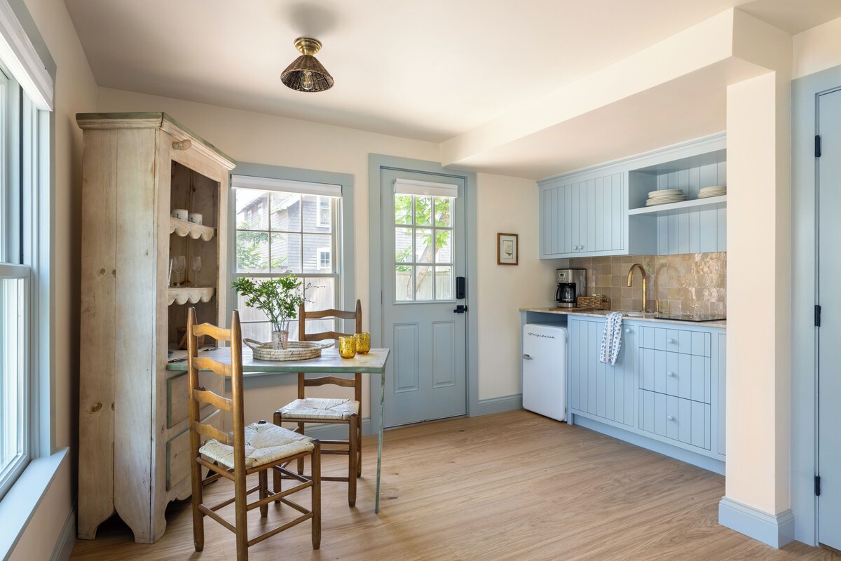 Una cocina con armarios de madera, una mesa de comedor con sillas y un refrigerador pequeño.