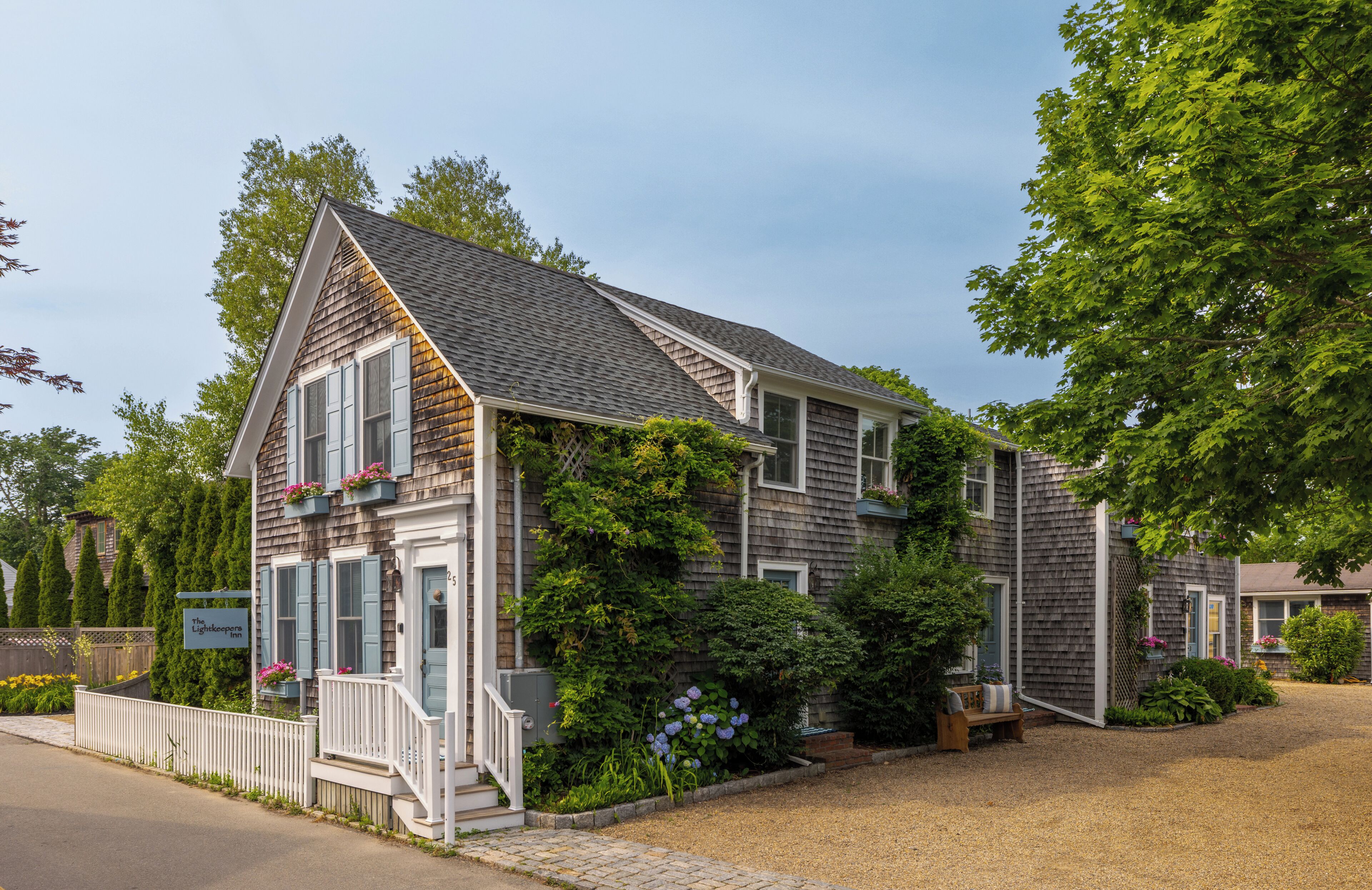 A two-story house with a front porch, a small garden, and a gravel driveway.