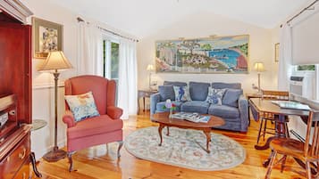 Ein Wohnzimmer mit einem roten Sessel, einem blauen Sofa, einem Couchtisch und einem Gemälde, das eine Küstenlandschaft zeigt.