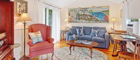 A living room with a red armchair, a blue sofa, a coffee table, and a painting of a coastal scene.