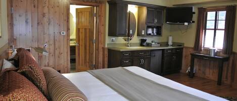 A bedroom with a large bed, wooden wardrobe, and a television in the adjacent room.