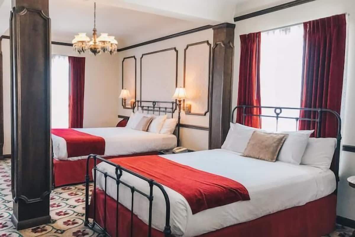 A hotel room with two beds, red curtains, a chandelier, and a patterned floor.