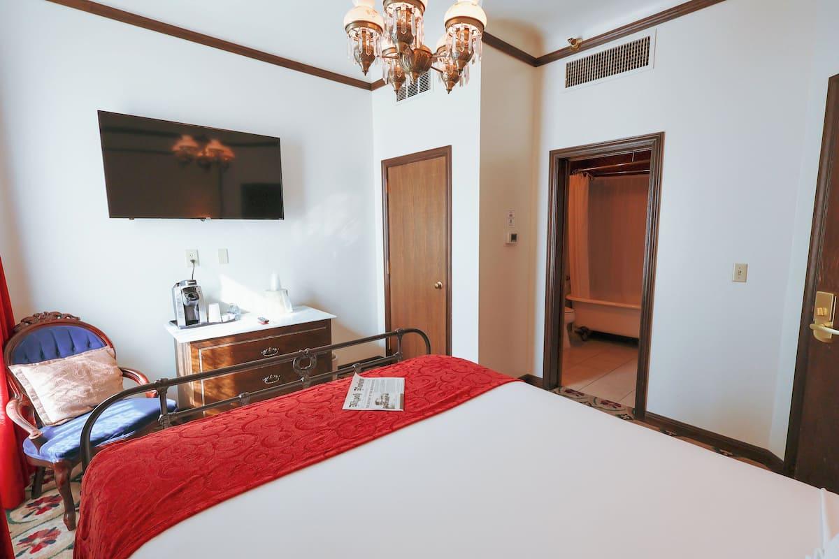 A hotel room with a bed, a television mounted on the wall, a wooden door, and a bathroom visible through an open door.