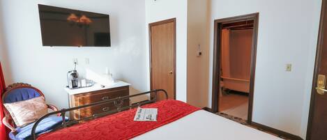 A hotel room with a bed, a television mounted on the wall, a wooden door, and a bathroom visible through an open door.