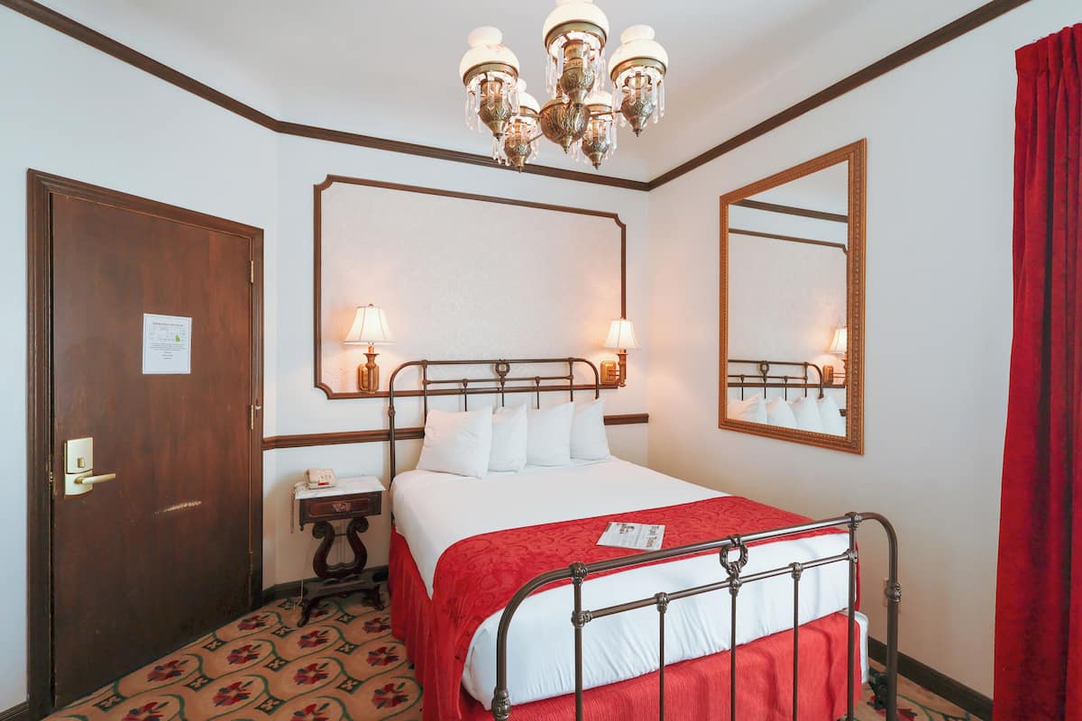 A hotel room with a bed, a nightstand, a mirror, and a chandelier.