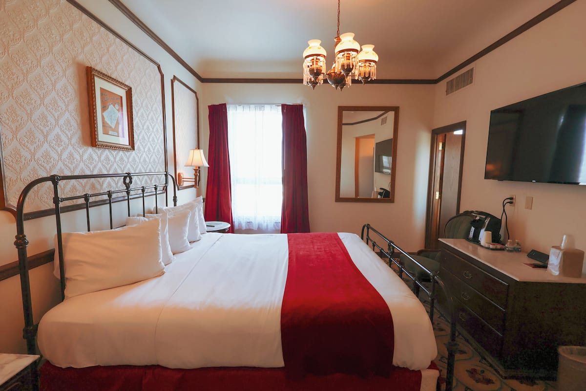 A hotel room with a large bed, a dresser, a television, and a chandelier.
