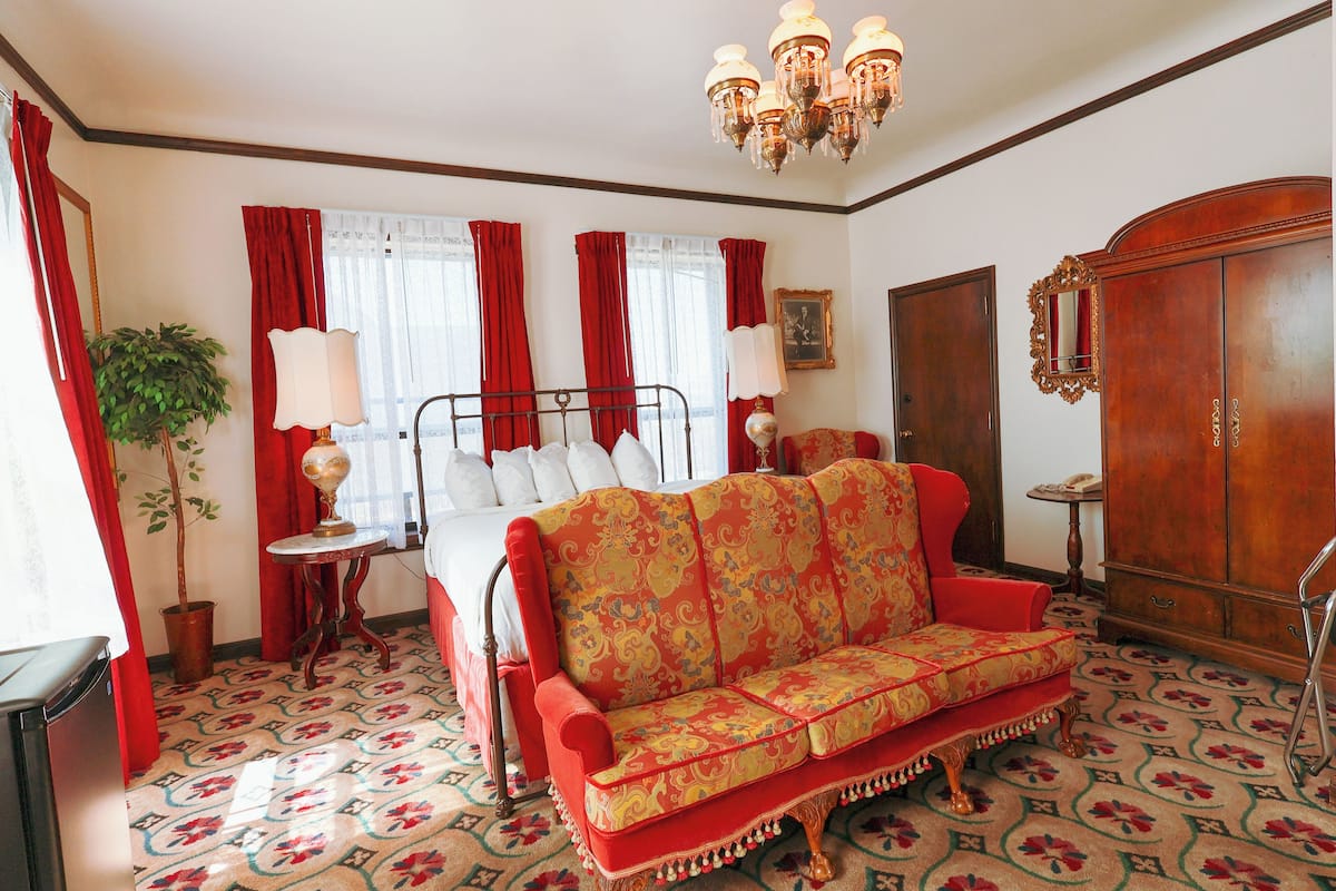 A room with a bed, a red sofa, a wooden wardrobe, and a chandelier.