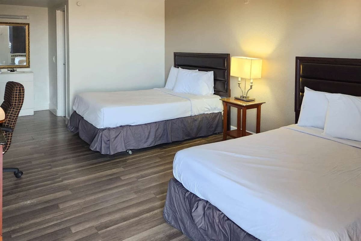 A hotel room with two beds, a wooden floor, a desk with a chair, and a mirror.