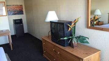A hotel room with a wooden dresser, a television, a lamp, a small refrigerator, and a painting on the wall.