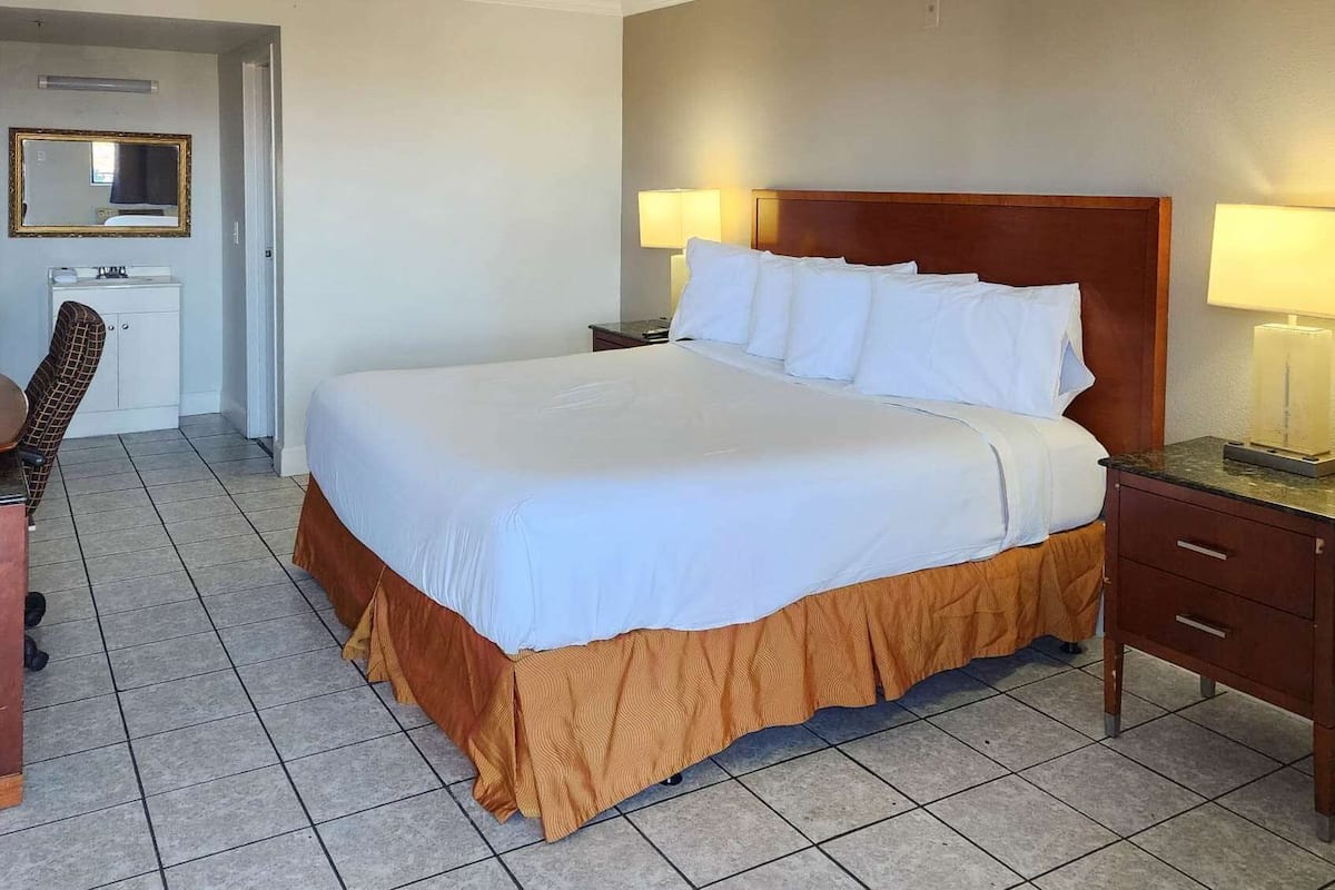 A hotel room with a large bed, two bedside tables with lamps, a desk with a chair, and a mirror on the wall.