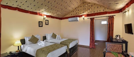 Quarto de hotel com duas camas, uma escrivaninha com cadeira, uma mesa de jantar com pratos e talheres, e um aparelho de ar condicionado na parede.