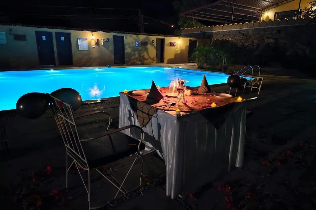 An outdoor pool area with a table set for dining, surrounded by chairs.