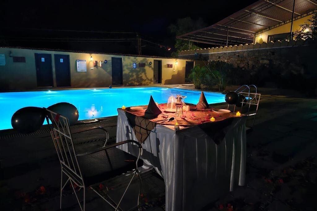 An outdoor pool area with a table set for an event, surrounded by a covered seating area.