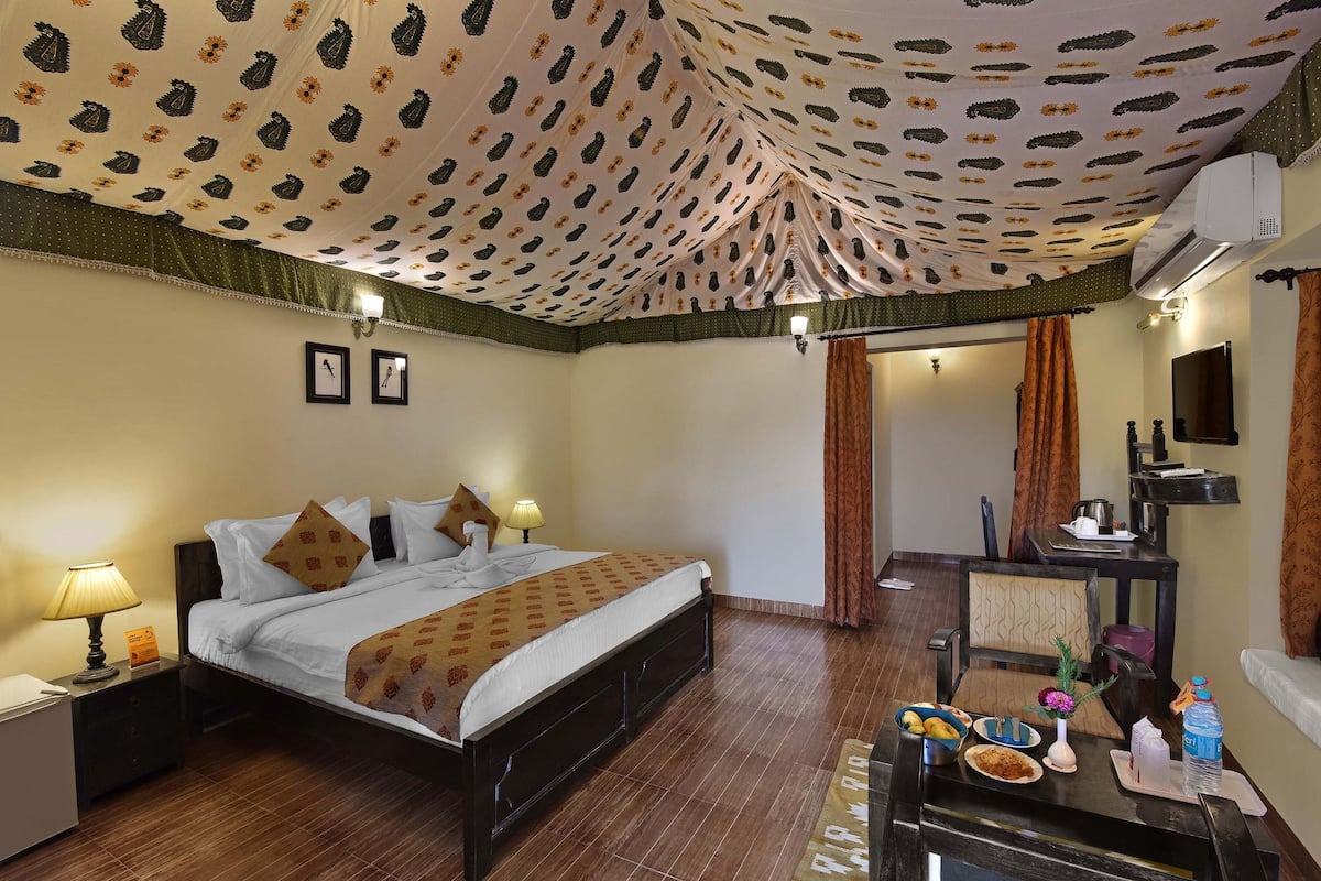 Habitación de hotel con cama, mesitas de noche, escritorio con silla, espejo y baño visible a través de una puerta abierta.