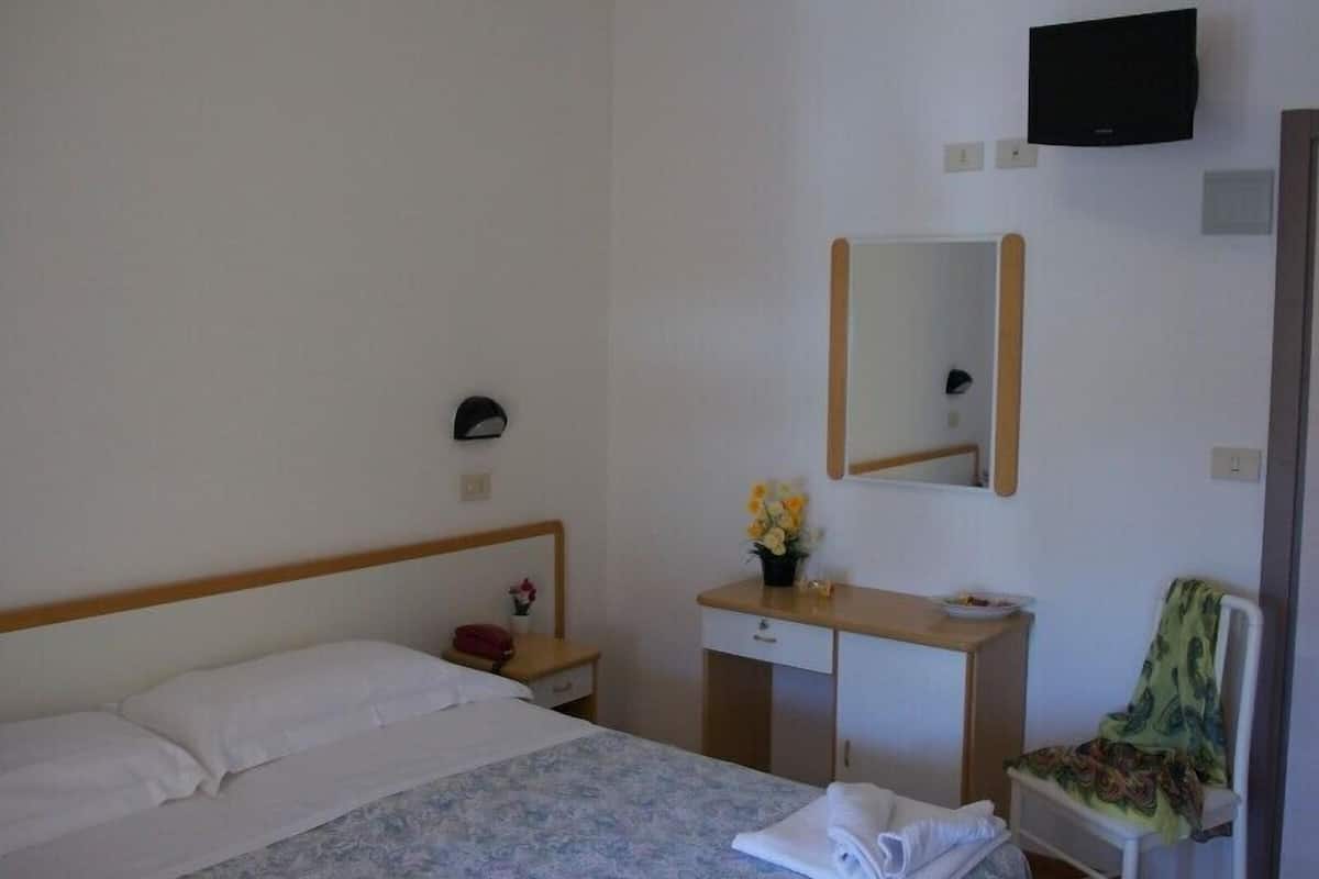 A hotel room with a bed, a desk with a mirror, a chair, and a TV mounted on the wall.