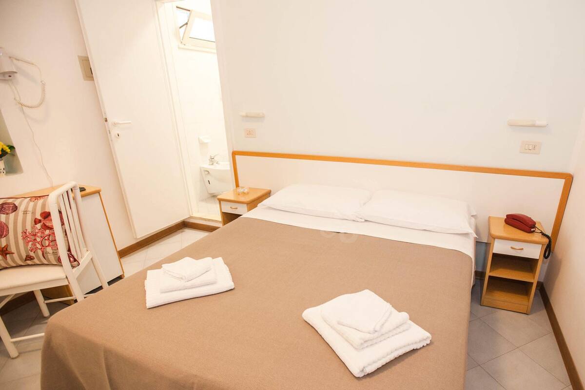 A hotel room with a bed, two bedside tables, a chair, a small table, and a telephone.