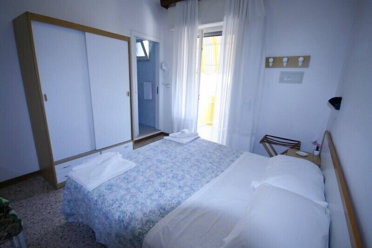 A bedroom with a bed, a wardrobe, a mirror, and a window with curtains.