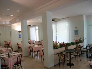 A dining area with tables and chairs, a flower arrangement, and a framed picture on the wall. - Hotel Massimo (Riccione)