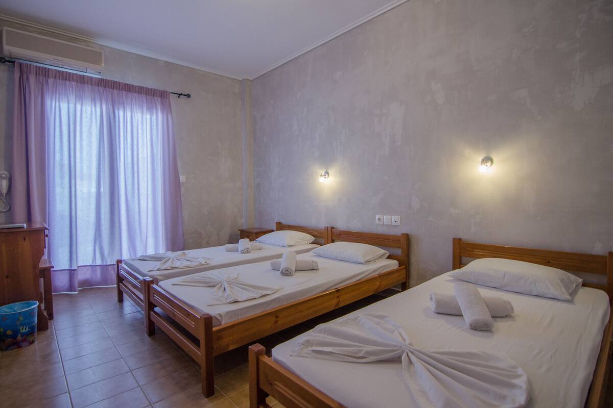 Ett hotellrum med två sängar i trä, båda med vita lakan och handdukar, en byrå i trä, ett skrivbord och en blå papperskorg.