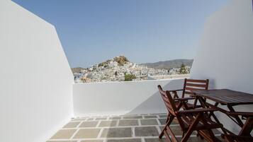 A balcony with a table and chairs, overlooking a white-washed village with a hill in the background.