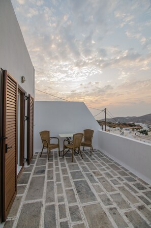 A balcony with a table and chairs, a white wall, and a view of the landscape. - George & Irene Hotel (Ios)