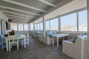A modern interior with a dining area, seating, and large windows offering a view of the landscape. - George & Irene Hotel (Ios)