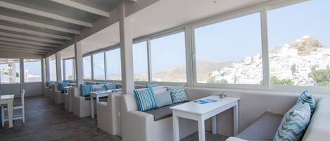 Un salón moderno y de planta abierta con muebles blancos, ventanas amplias que ofrecen vistas a una colina blanca y un diseño limpio y minimalista.