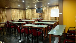 A conference room with tables and chairs, a ceiling fan, and a flat-screen TV. - Hotel Dreams (Thiruvananthapuram)