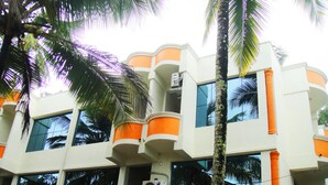 A multi-story building with balconies, large windows, and palm trees. - Hotel Dreams (Thiruvananthapuram)