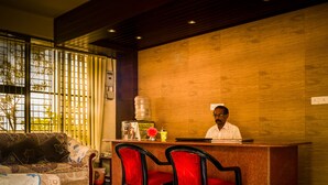 A reception area with a wooden wall, a reception desk, a sofa, and a chair. - Hotel Dreams (Thiruvananthapuram)