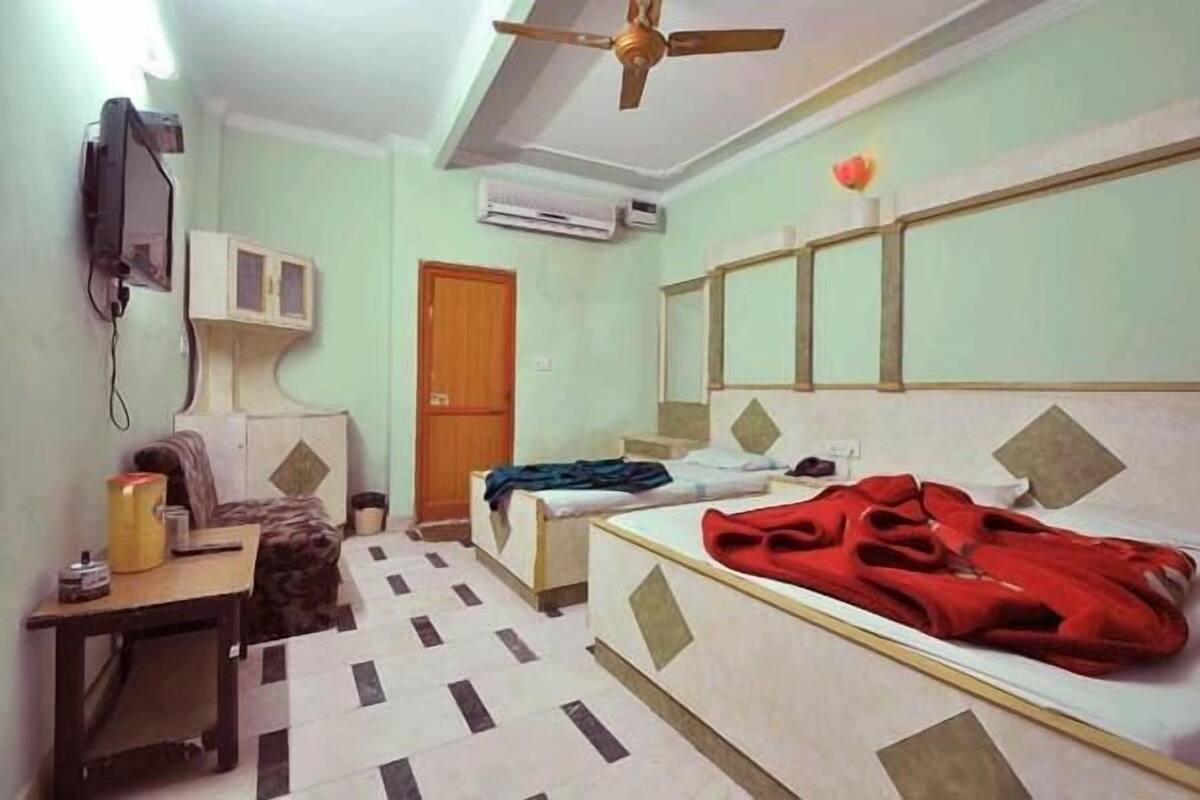 A room with a bed, a desk, a chair, an air conditioning unit, and a television mounted on the wall.