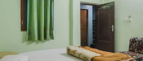 Une pièce avec un lit, un rideau vert, une porte en bois et une chaise à motifs floraux.