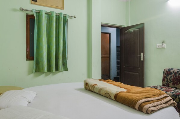 A room with a bed, a green curtain, a wooden door, and a floral-patterned chair.