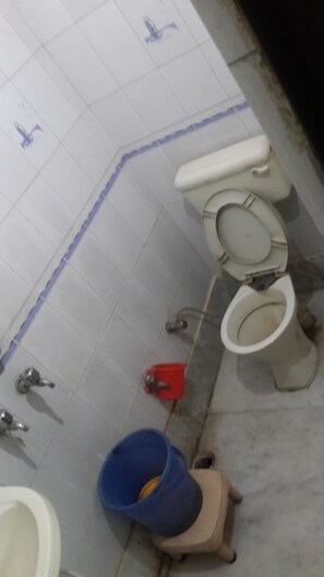 A tiled bathroom floor with a toilet, bidet, and a blue bucket. - Hotel Neha Inn (New Delhi)