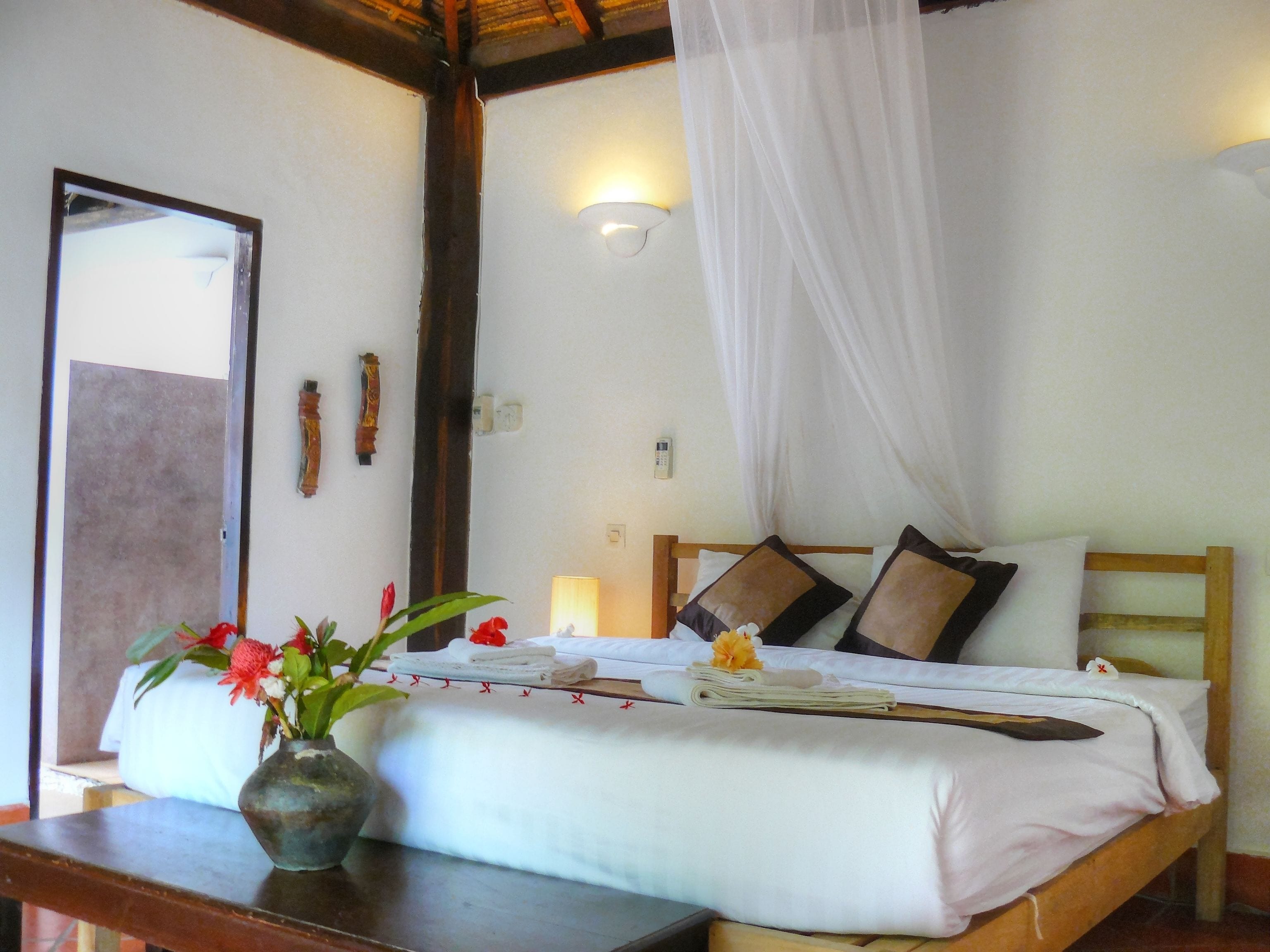 A bedroom with a bed, a bedside table with a vase of flowers, a nightstand, and a wall-mounted lamp.