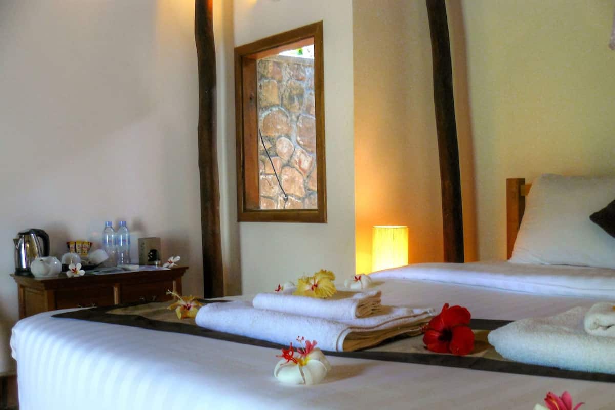 Habitación de hotel con cama, mesita de noche, lámpara y ventana con vista a un muro de piedra.