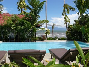 Zona de piscina con sillones, una mesa y vista al océano.