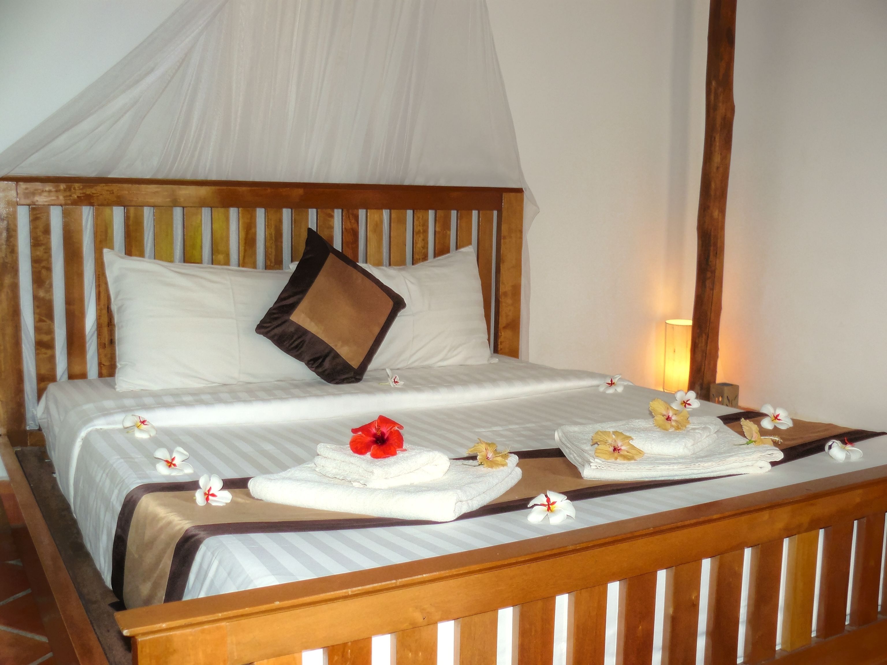 A bed with a canopy, pillows, and towels with flowers.