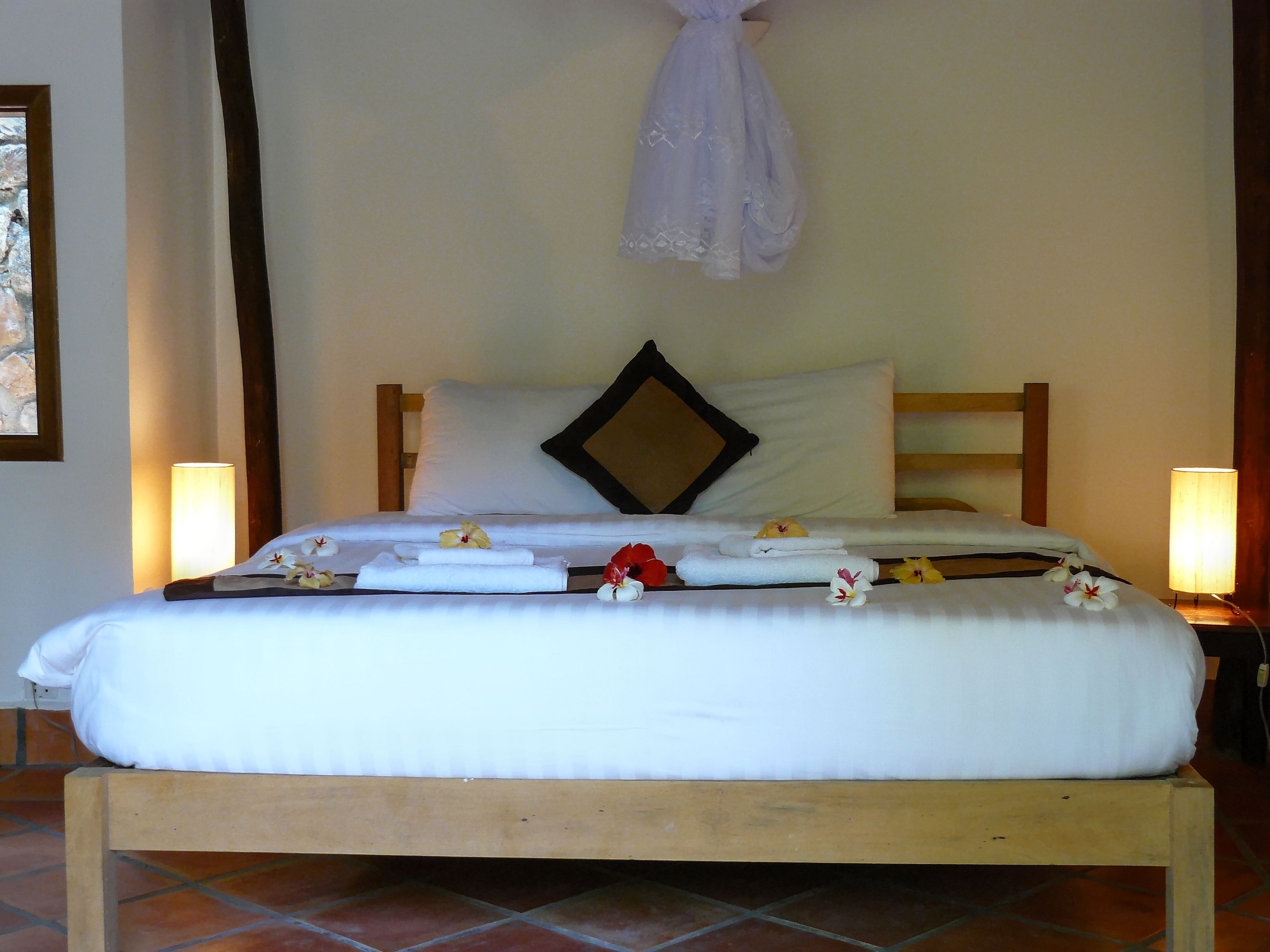 A neatly made bed with white linens, a wooden headboard, and two bedside lamps.