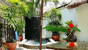Un pequeño jardín con fuente, plantas en macetas y una estructura de techo de paja.