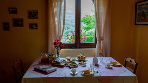 Une table à manger dressée avec des assiettes, des verres et un pichet, donnant sur un paysage verdoyant par la fenêtre et sur une porte.