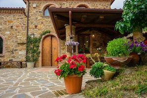 A stone building with a wooden door and a covered entrance. There are potted plants and flowers in front of the building.